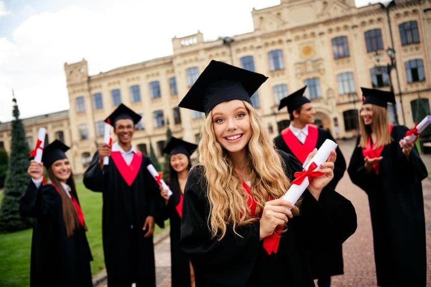 Vidám fiatal diplomások csoportja, akik a szabadban ünnepelik tudományos eredményeiket.