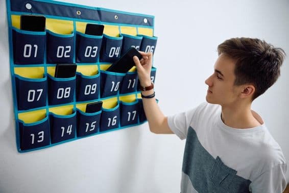 Diák a falra akasztott mobiltelefon-szervezőben hagyja az okostelefonját.