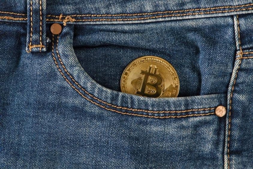 Egy arany bitcoin érme fekszik egy farmernadrág zsebében.