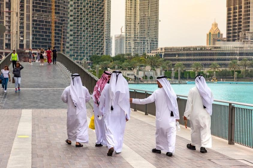 Hagyományos fehér ruhát viselő arab férfiak sétálnak Dubai belvárosában.