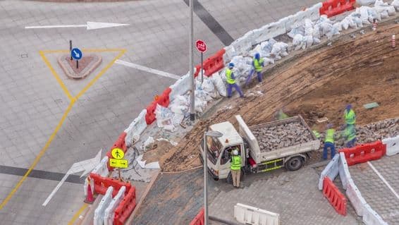 Járdajavítási folyamat sok építőmunkással és berendezéssel, akik járdát és betont bontanak.