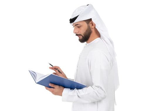 Fiatal arab tanár áll és ír a könyvbe.