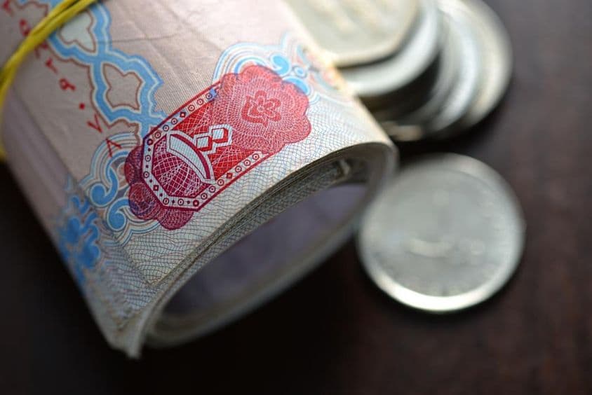 Feltekercselt és néhány érmével együtt elhelyezett egyesült arab emírségekbeli dirham.