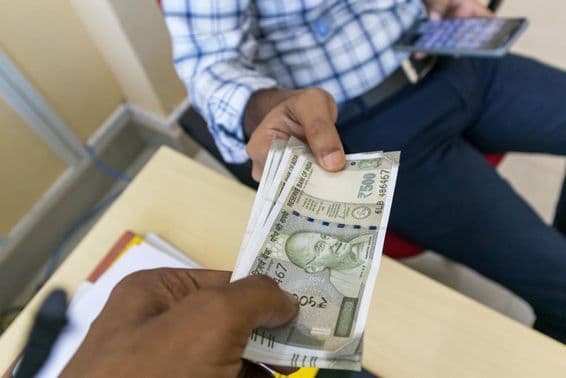 Egy személy pénzt (500 rúpiás indiai bankjegyet) ad egy másik személynek.