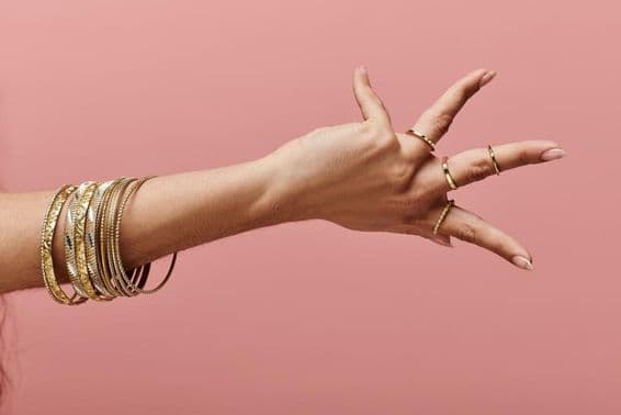 Indiai nő elegáns pózban mutatja a kezén az arany karkötőket.