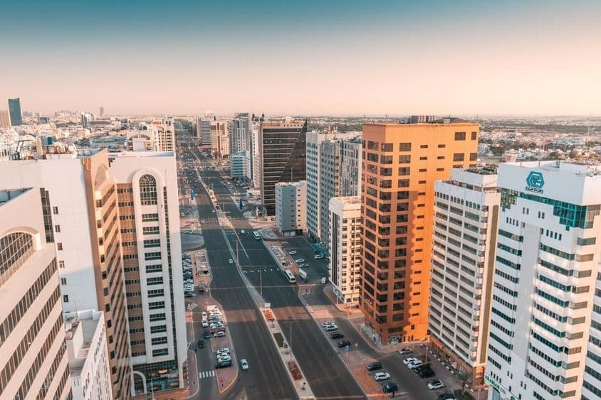 Abu Dhabi, légifelvételek egy széles utcáról, ahol autóforgalom halad át a felhőkarcolók között.