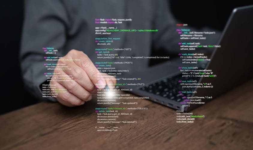 Egy programozó kezei egy laptopon, programozási kóddal.