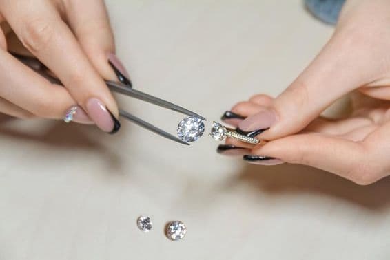 Egy ékszerész női kezei egy drágakövet tartanak.