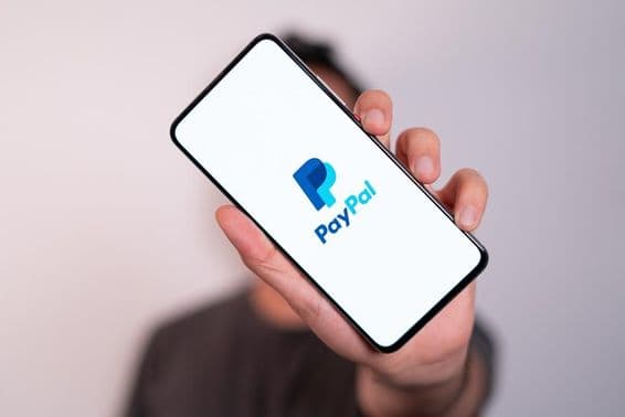 Egy férfi egy telefont tart a kezében a telefon képernyőjén pedig a PayPal logó látható.