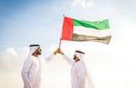 Arab férfiak, akik kandorát viselnek, sétálnak a sivatagban, kezükbe zászló.