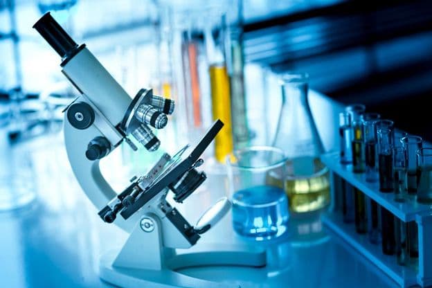 Mikroszkóp az asztalon kémiai csővel és üvegeszközökkel.