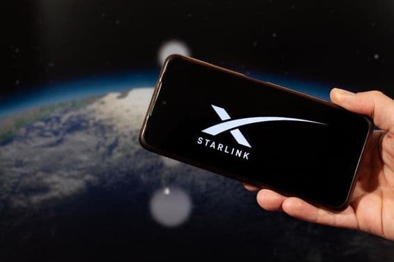 Egy férfi kéz tart egy okostelefont a jobb kezével Starlink logóval.