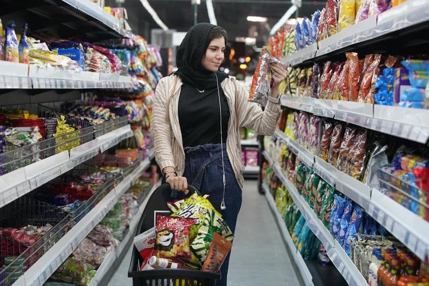 Egy fiatal arab hölgy egy szupermarketben nézi a rágcsálnivalókat.