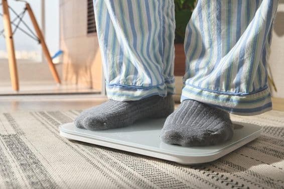 Férfi csíkos pizsamában áll egy fehér digitális mérlegen