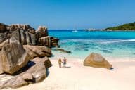 Két utazó sétál az Anse Cocos Beach puha fehér homokján Seychelle-szigeteken.