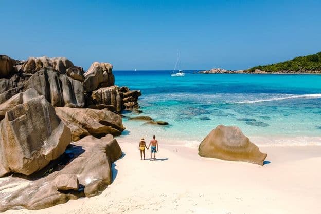 Két utazó sétál az Anse Cocos Beach puha fehér homokján Seychelle-szigeteken.