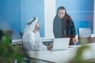 Férfi és nő hagyományos ruhában dolgoznak egy dubai üzleti irodában.