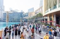 Turisták és helyiek sokszínű tömege sétál a Dubai Mall előtti forgalmas vízparti sétányon.