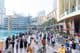 Turisták és helyiek sokszínű tömege sétál a Dubai Mall előtti forgalmas vízparti sétányon.